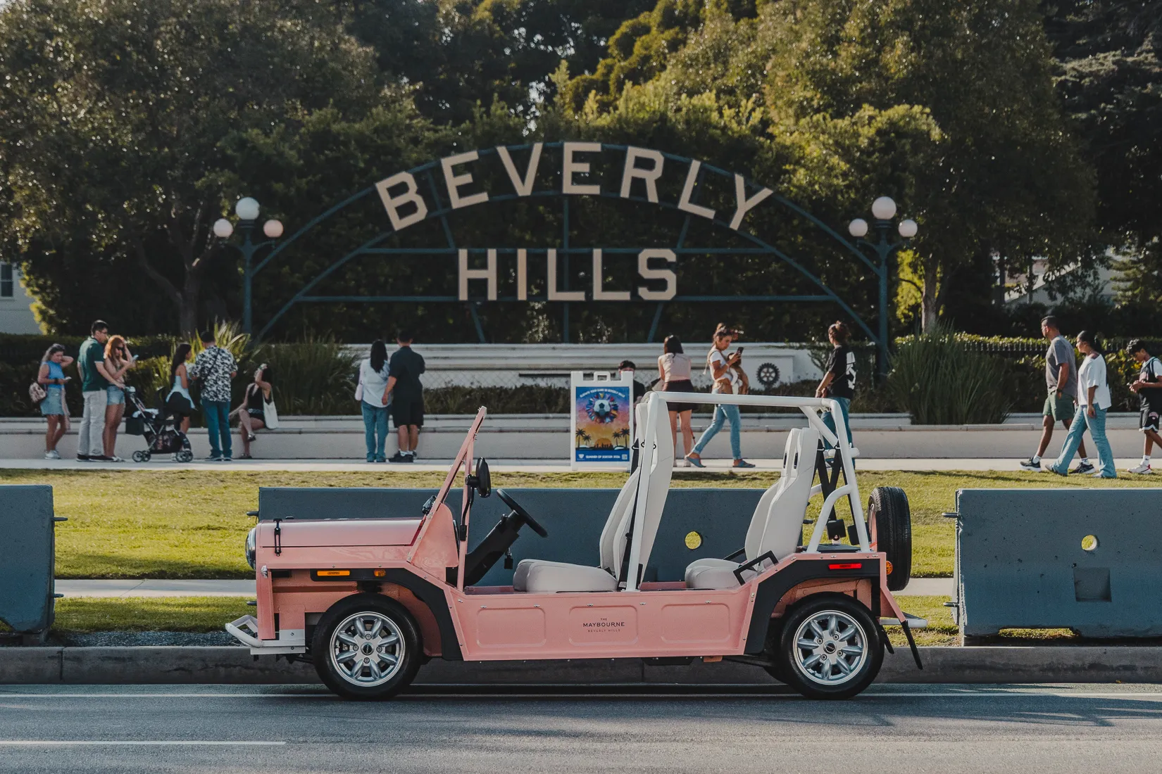 A pink electric Moke parked beneath the Beverly Hills sign