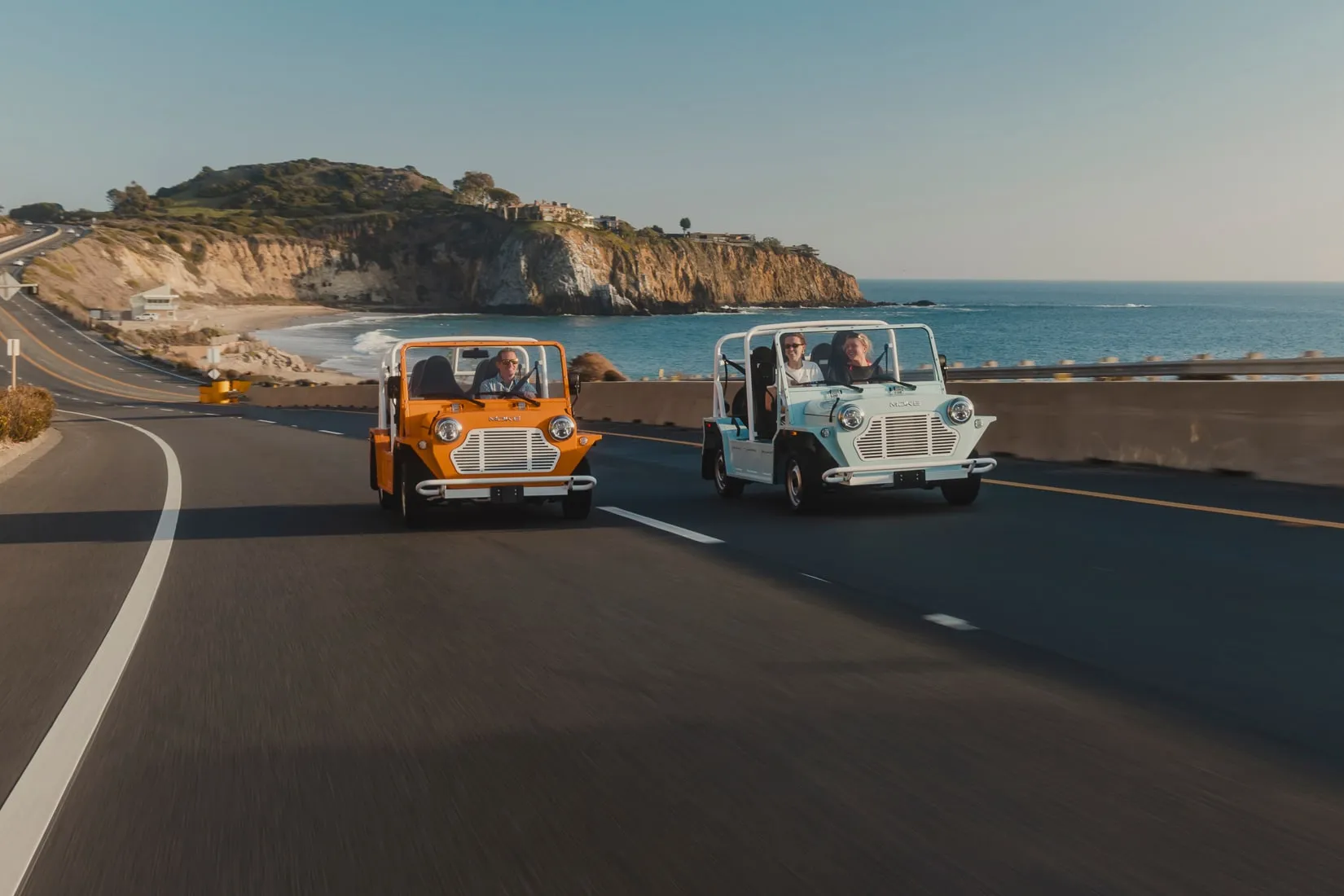 Two Mokes driving a coastal highway above the Pacific