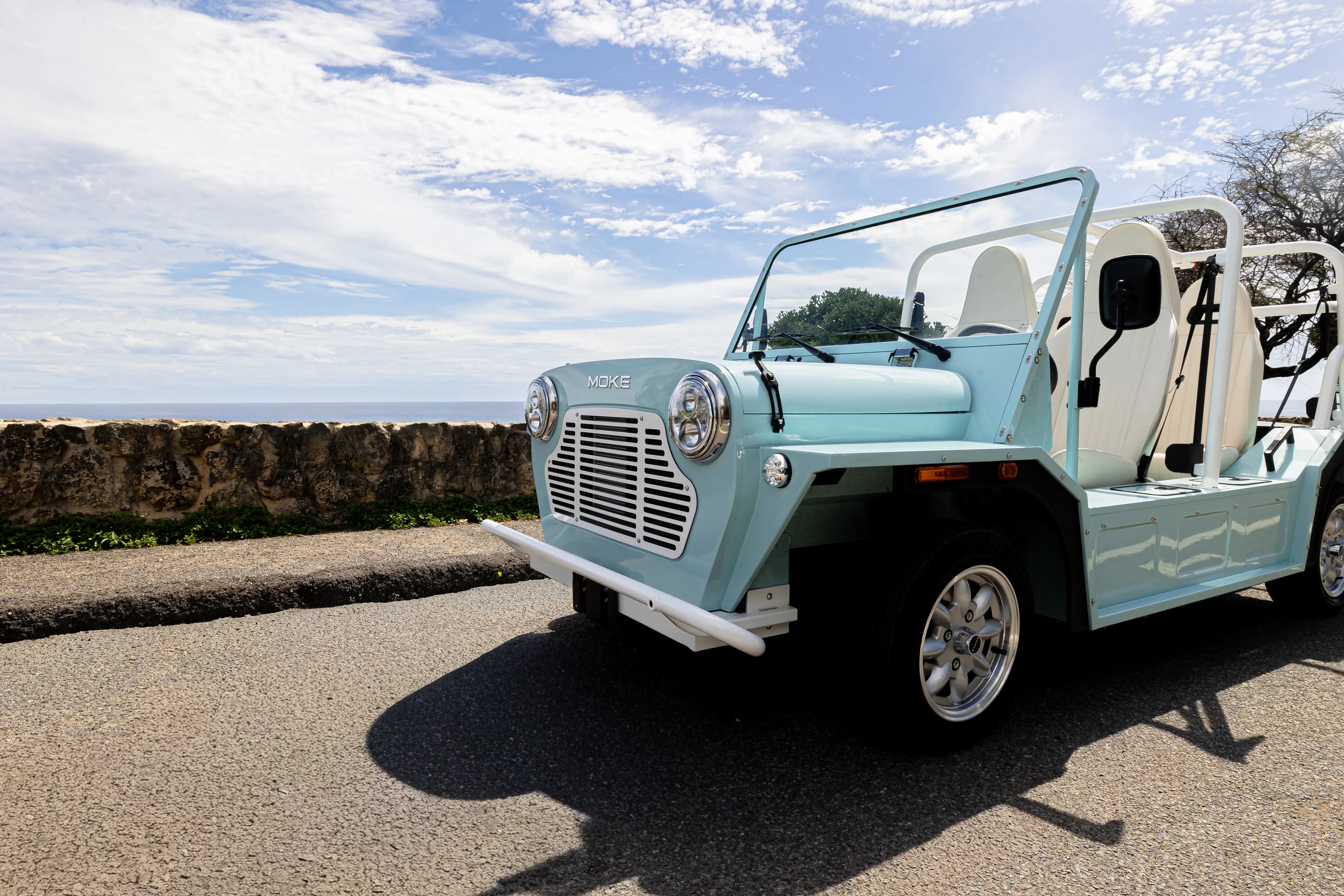 A pale blue Moke on a coastal road under a wide sky