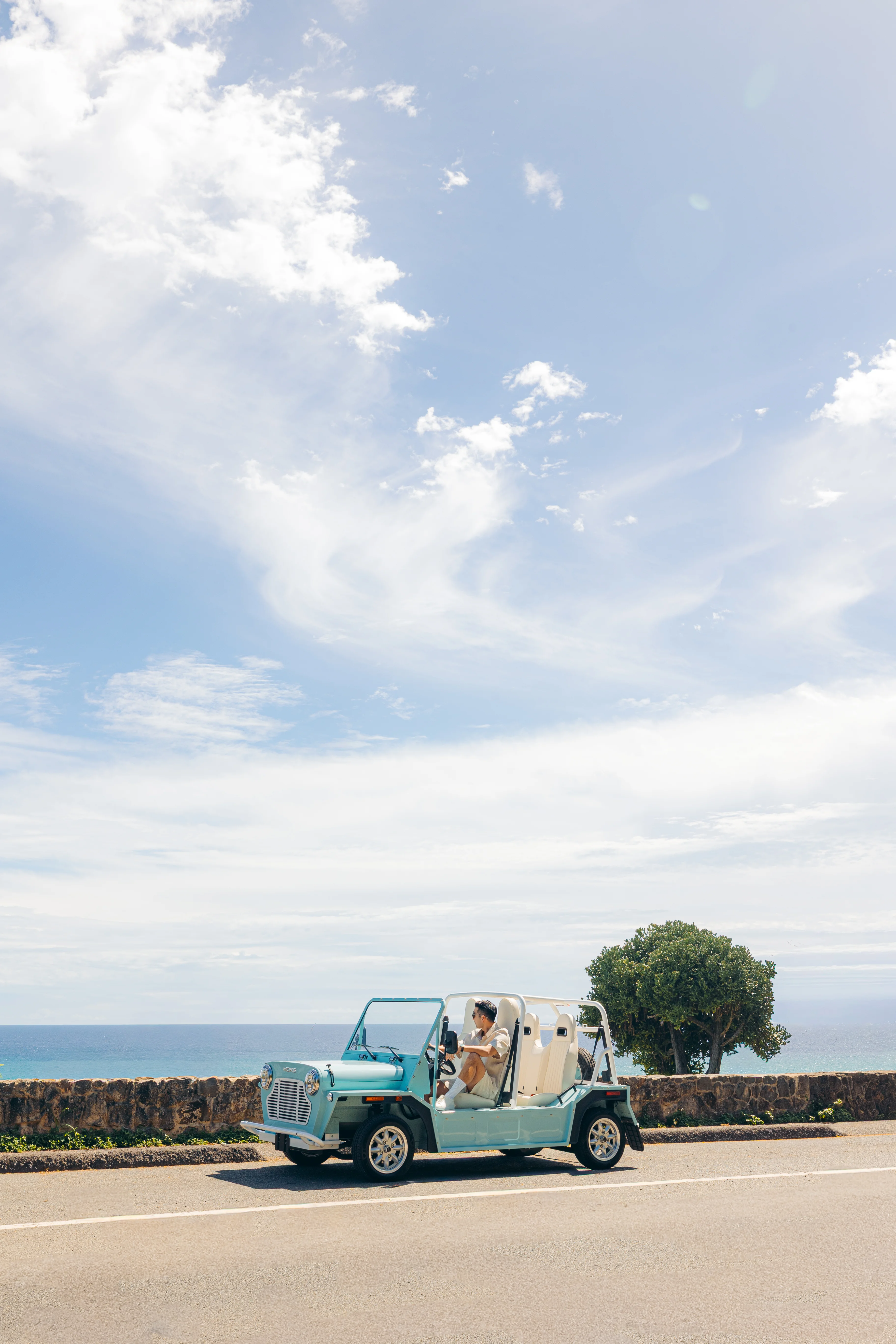Moke mid-drive on the coast road under a wide soft sky